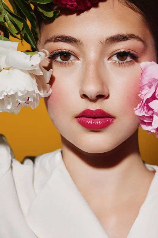 Close-up portrait of creative woman with bright pink lipstick and floral makeup on yellow background. Concept for beauty, fashion, and artistic expression.