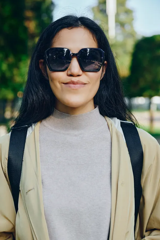 Sunglasses, woman wearing casual jacket and backpack in a sunny park outdoor scene, smiling, street fashion vibe, candid wellness and relaxed travel style, daylight glow and fresh air