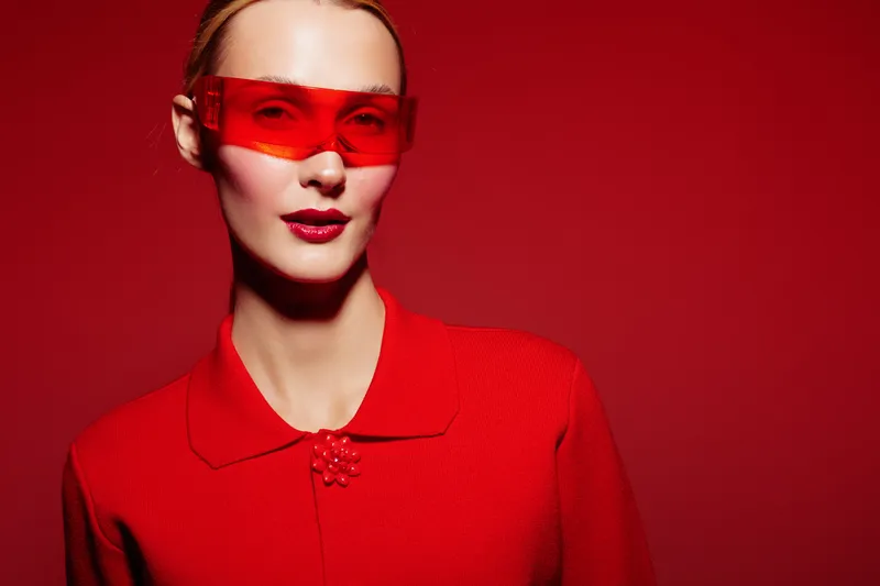 Stylish woman in red outfit and red sunglasses poses against red background. Fashion portrait with bold color contrast and modern accessories. Concept of style, confidence, and elegance.