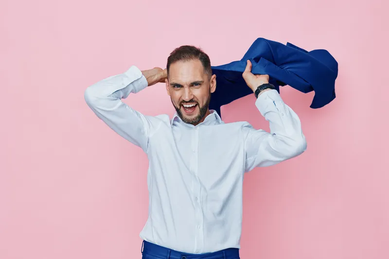 A professional man on a pink studio backdrop with an isolated colored setting, exuding energy as he grips a blue jacket, signaling momentum, focus, and confident business vibe.