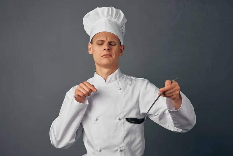 Шеф-повар мужского пола пробует на вкус блюда профессионального ресторана