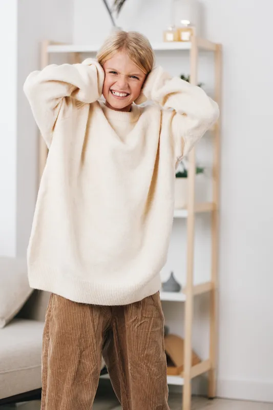 Authentic lifestyle image of a young child at play, wearing a soft oversized sweater, capturing candid joy and everyday comfort in a cozy living room.