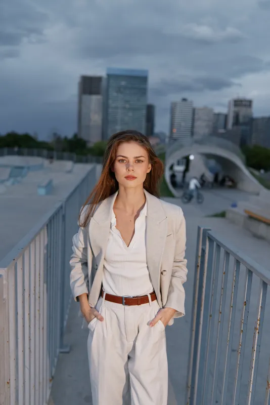 confident woman in beige suit walking outdoors with urban skyline background, professional business attire and serious expression