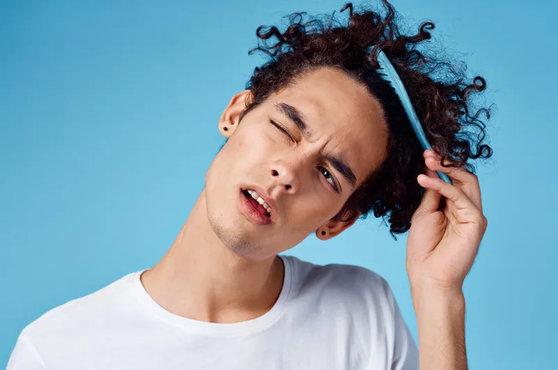 Парень-модель с расческой в руке и кудрявыми волосами на синем фоне