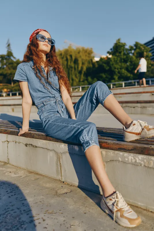 Lifestyle woman in modern boho-western denim street style poses confidently outdoors wearing sunglasses and casual sneakers, inspired by film color tones and urban vibes.