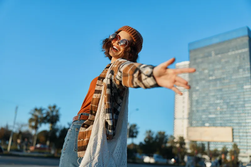 Woman smile urban lifestyle portrait of joyful casual outdoor scene with sunglasses and beanie, candid authenticity and golden hour glow conveying mindful living and emotional storytelling.