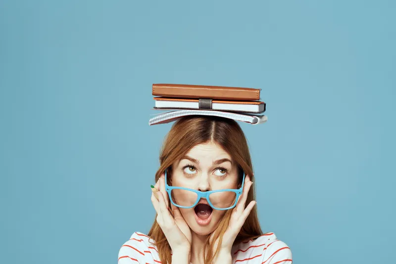 Студентка с книгами на голове, наука, образование, синий фон, эмоции, жестикуляция руками