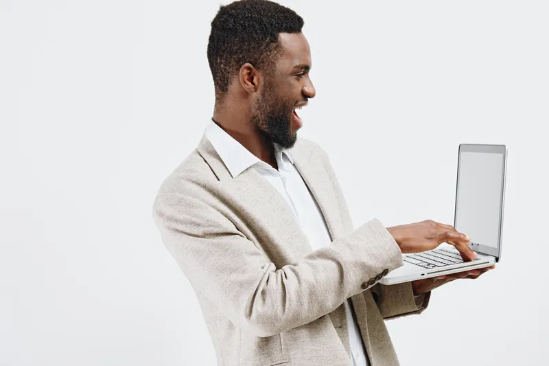 Smiling man using laptop computer with white background, casual beige blazer, beard, cheerful expression, working from home, technology, lifestyle, modern professional, male, adult, positive mood, stu