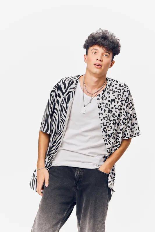 young man wearing casual animal print shirt and white t-shirt, posing relaxed with hand in pocket against white background, curly hair, stylish urban look