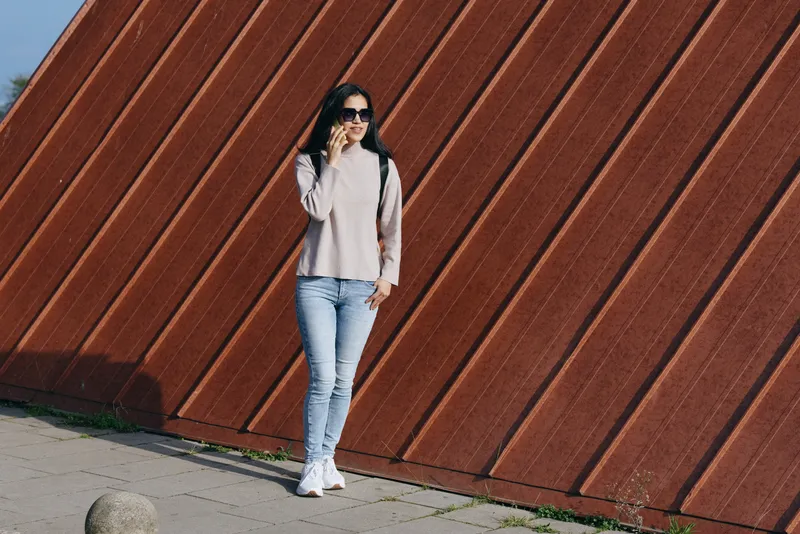 Fashion, woman, outdoor, streetwear, casual, denim, sunglasses, urban scene featuring a stylish figure beside a diagonal wall in daylight, wearing sweater and sneakers for an urban lifestyle shot
