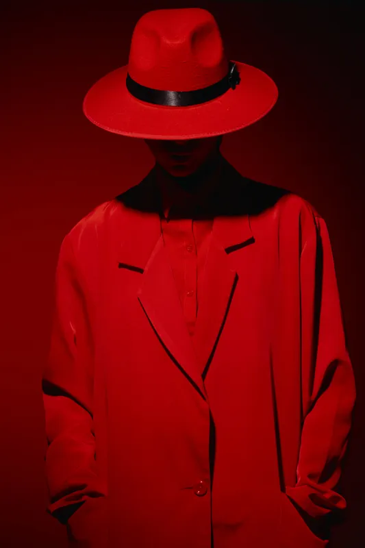 Stylish model in a striking red hat and matching oversized coat. Mysterious mood with strong shadow over face. Creative fashion concept focusing on silhouette and bold color.