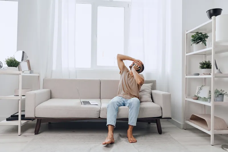 Distressed man sitting on a couch, holding his head in frustration. The modern, bright interior reflects an atmosphere of stress and uncertainty.