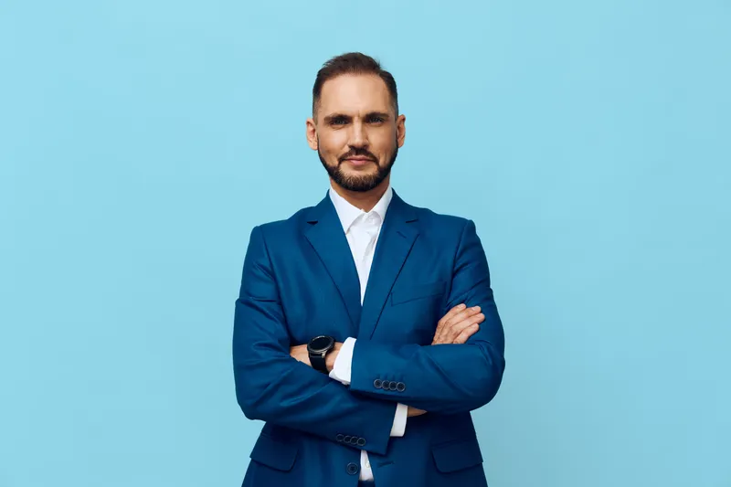 A confident business professional stands against a solid colored backdrop, projecting focus and calm. Strong posture, clear gaze, and poised demeanor suit corporate communications.