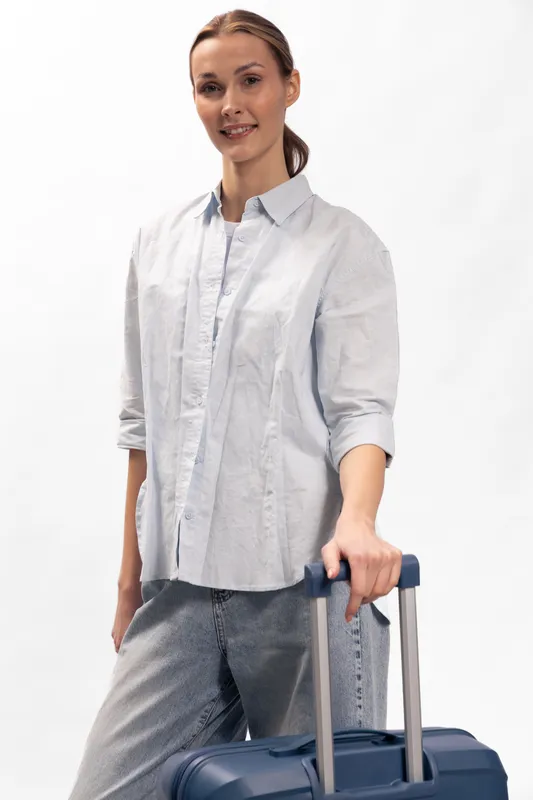 Smiling woman in casual shirt holding suitcase handle, ready for travel. Isolated on white background. Concept of tourism, vacation, business trip, and female traveler.