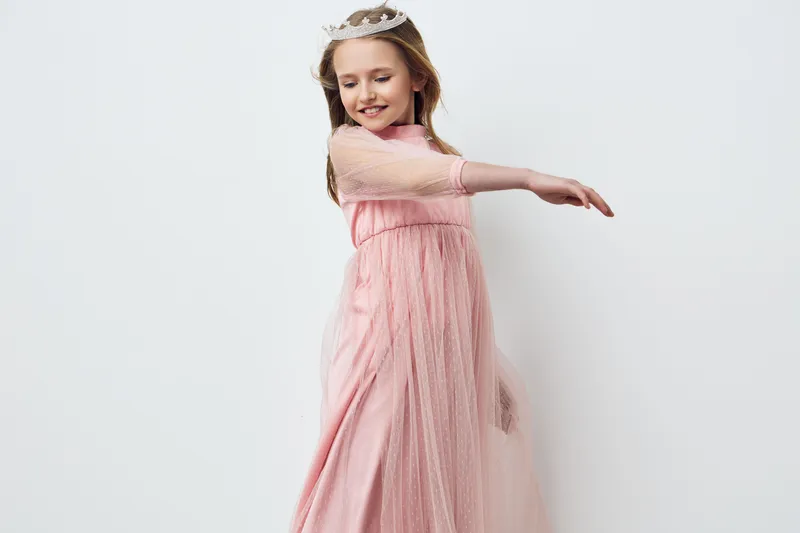 A joyful girl in a pink tulle dress dancing gracefully against a minimalistic white background, showcasing innocence and happiness