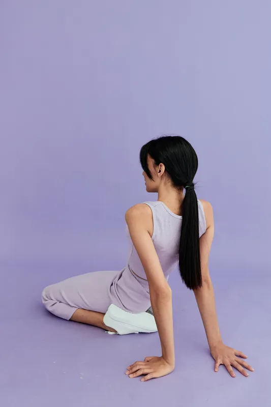 woman stretching on floor in lavender activewear with white sneakers against mauve background, fitness, flexibility, calm, wellness, indoor exercise