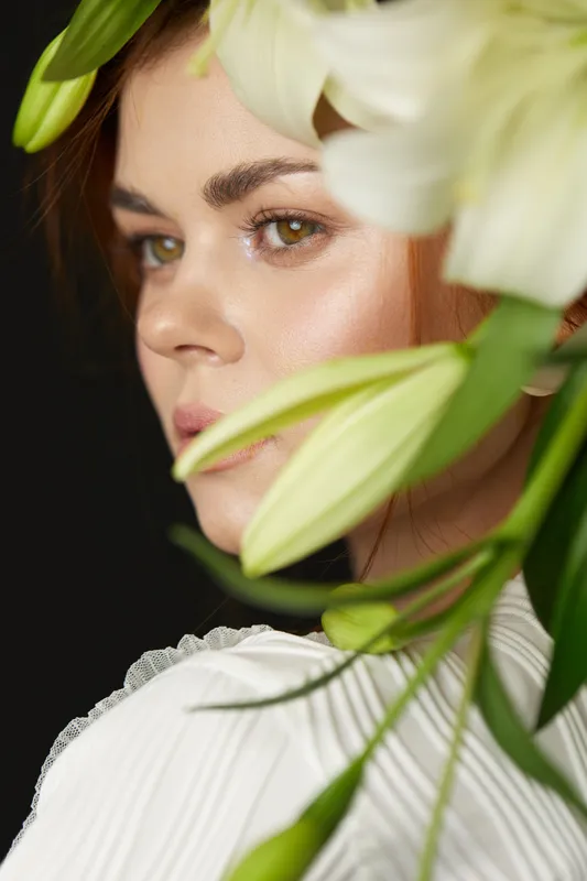 Beautiful woman with green eyes and long brown hair surrounded by white lilies, showcasing elegance, natural beauty, and fresh emotions in a floral portrait