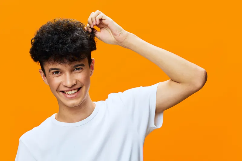smiling man in white t-shirt with curly hair standing against bright orange background, happy expression, casual style, studio portrait, young adult male