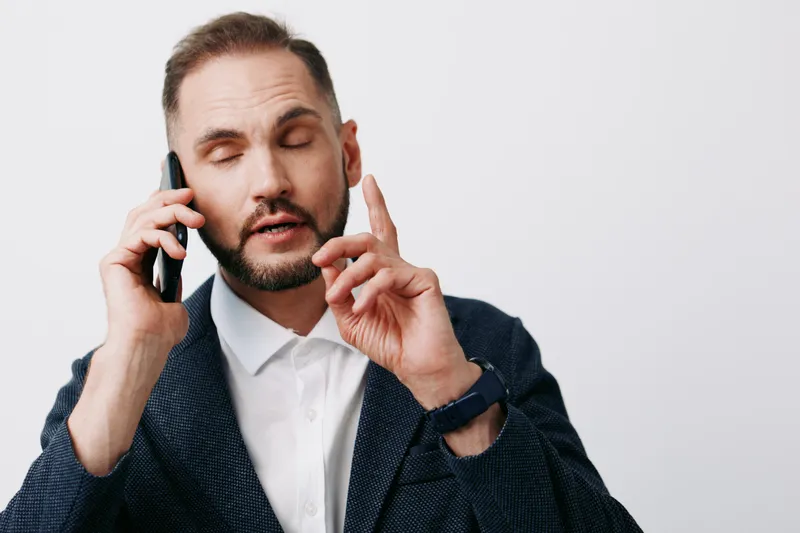 A professional man in business attire speaks on a mobile phone against an isolated colored background, illustrating focus, calm confidence, and poised communication during a work call.