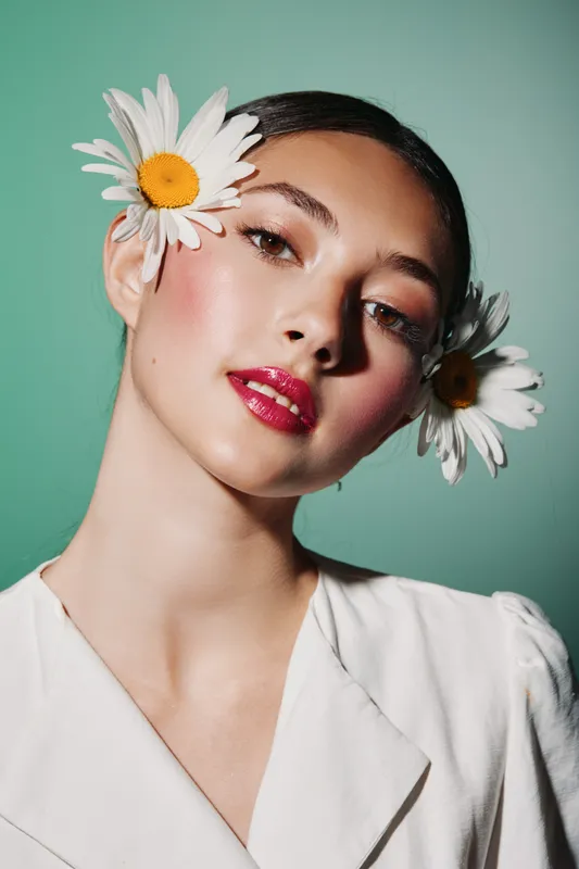 Beauty portrait of a young woman with makeup, coral lipstick, and flowers in her hair on a green background. Creative fashion concept with fresh natural elements.