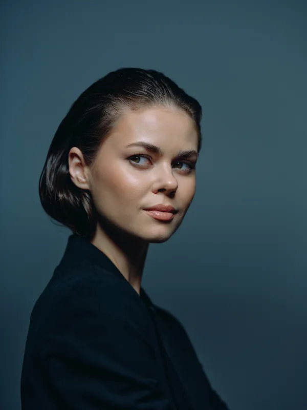 Portrait of a young woman with short dark hair and blue eyes wearing a black blazer against a dark background