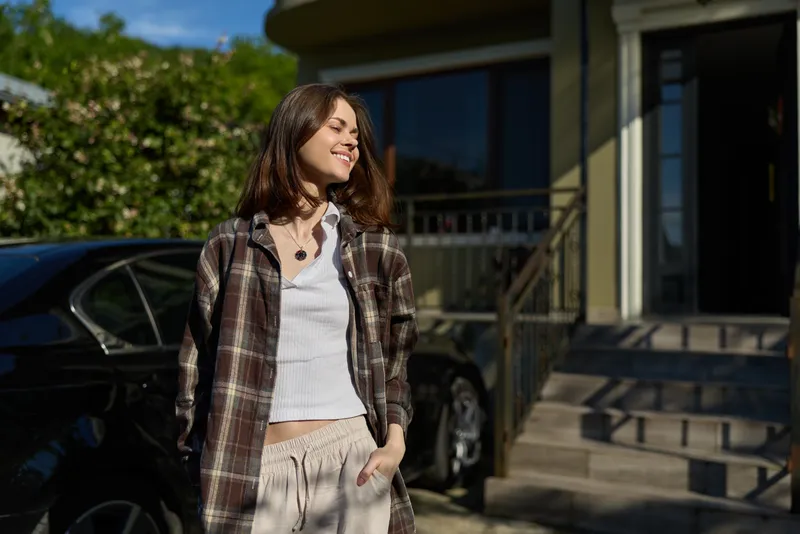 Cheerful woman outdoors, casual outfit, smiling in sunlight, relaxed stance, warm breeze, natural colors, urban street scene, candid lifestyle