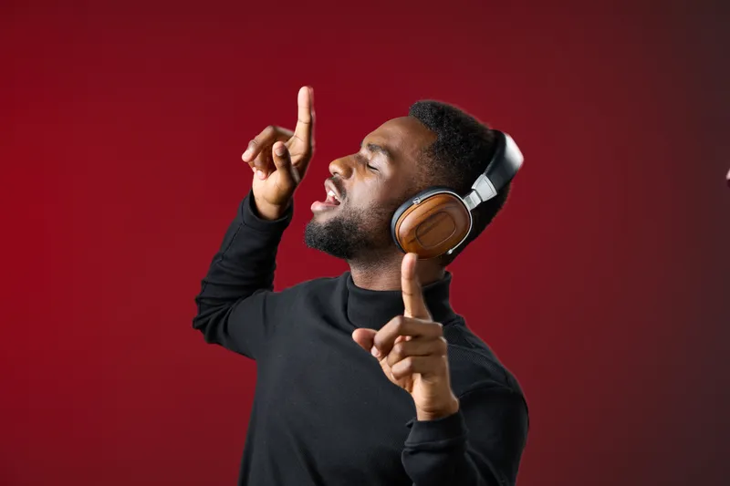 Joyful young African man enjoying music with headphones, expressing happiness and movement against a vibrant red background