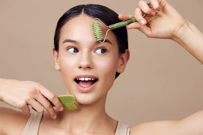 Young woman enjoying facial massage with jade roller and gua sha tool, promoting skincare routine and self care for healthy skin