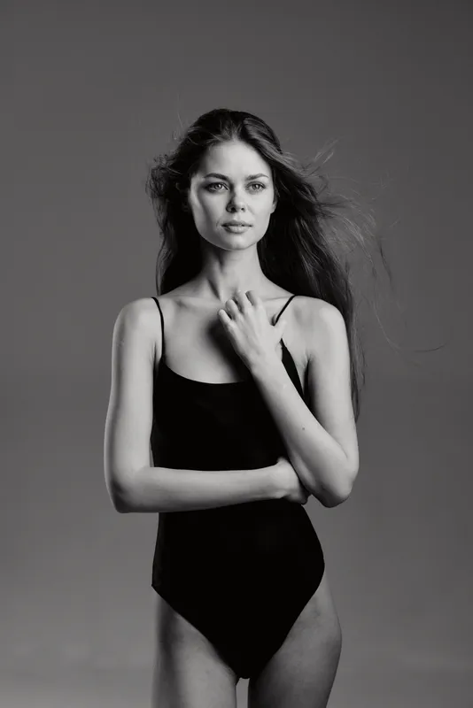 Black and white portrait of a woman in a black swimsuit with natural hair, posing thoughtfully against a plain background.