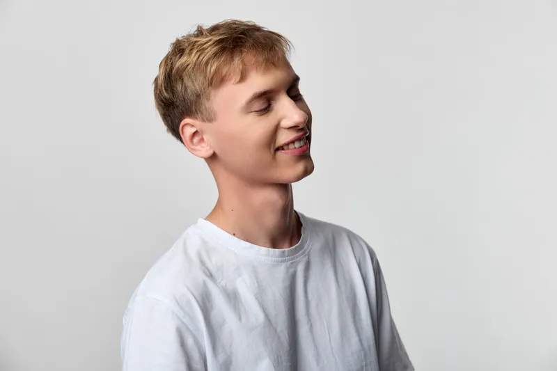 Smiling man in a white shirt in a studio setting, casual and relaxed, showcasing natural happiness and calm confidence for lifestyle, fashion or stock photography projects