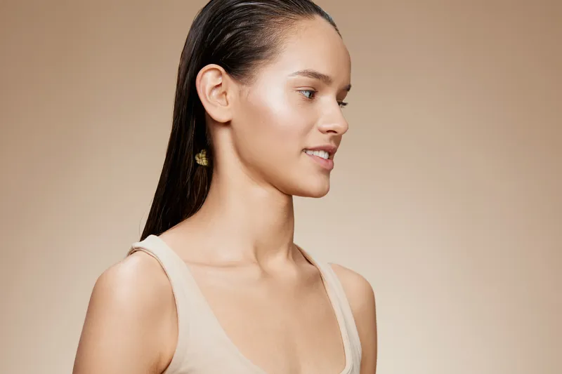 Beautiful young female model with sleek hair and natural makeup against a neutral background, conveying a sense of calm and confidence, ideal for beauty and skincare concepts
