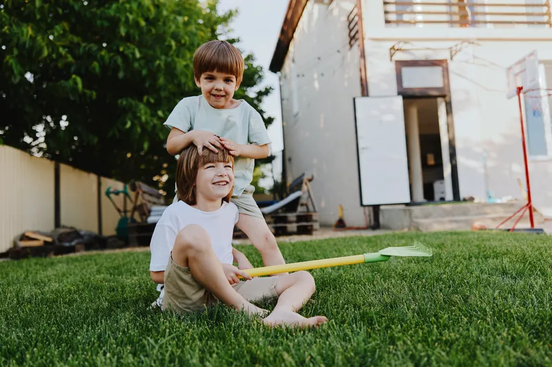 Playful children enjoying a sunny day in the garden, laughing and having fun together, surrounded by lush greenery and a cheerful atmosphere.