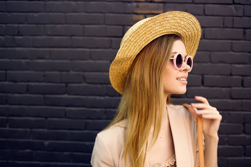 Элегантная женщина в солнцезащитных очках на прогулке по улице, городской стиль, кирпичная стена на заднем плане