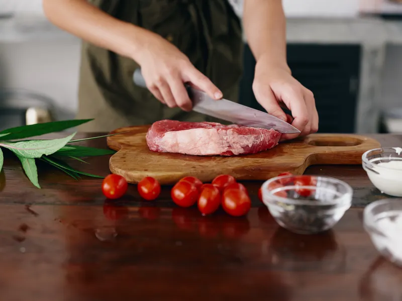 Женщина с ножом в руке нарезает свежее мясо стейка для жарки на кухне