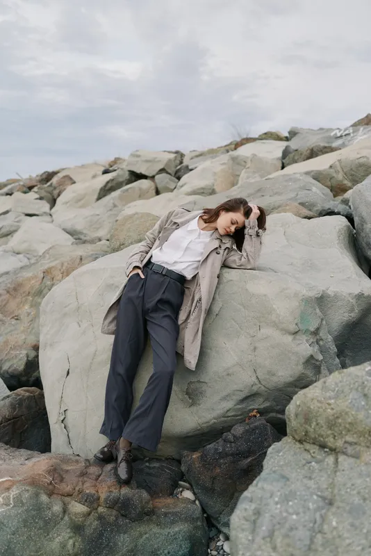 Young woman in casual clothes leans on large rock outdoors. Overcast sky and rocky landscape create calm natural mood. Concept of relaxation, nature, and thoughtful moment.