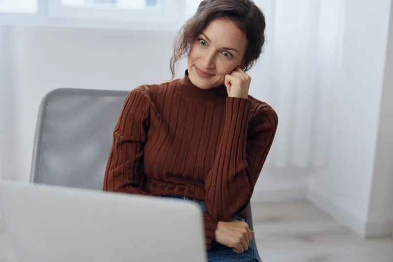 Забавная, милая, сбитая с толку, взволнованная, шокированная молодая кудрявая симпатичная женщина разговаривает с друзьями по видеоконференции, используя ноутбук на коленях, получает неоднозначные…