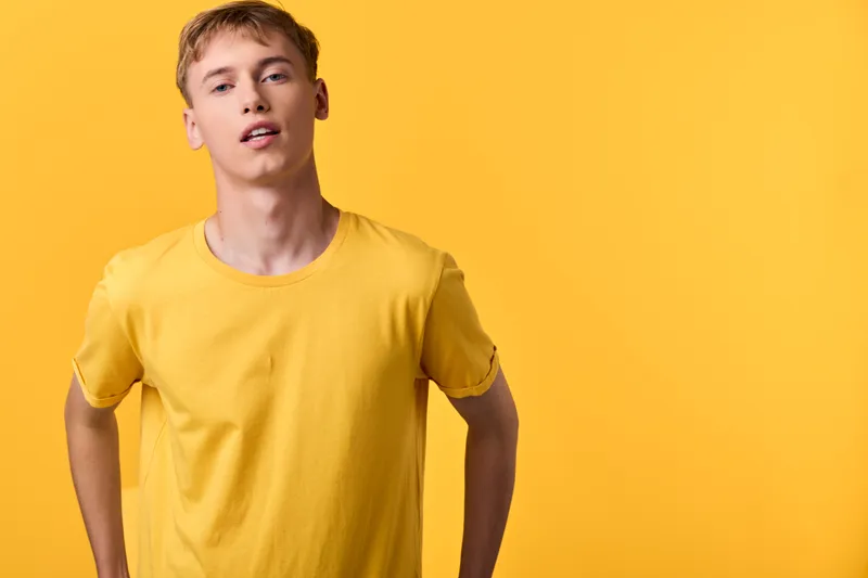 Young man in a bright yellow t shirt poses confidently against a yellow background, creating a bold color block scene that conveys energy, playfulness, and a contemporary streetwear vibe.