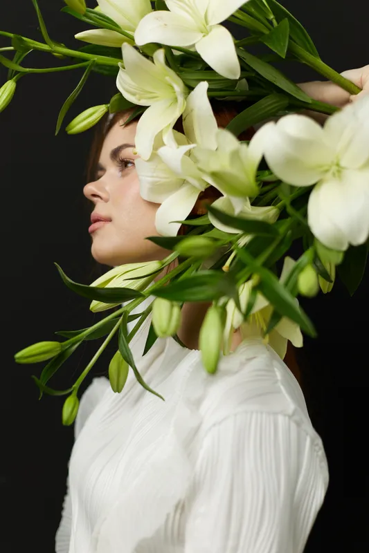 Elegant female portrait with white lilies, showcasing beauty and tranquility against a dark background, embodying a floral concept and a serene emotion