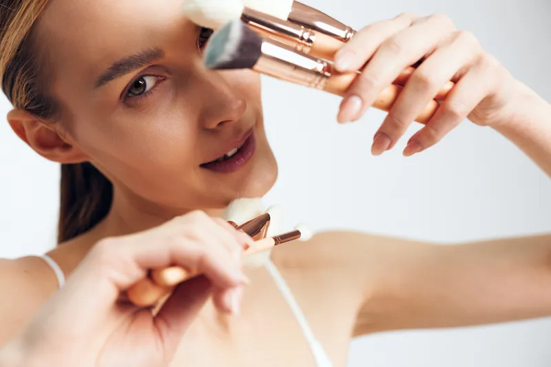 Woman applying makeup with lip cosmetics, closeup on a soft studio background. Beauty routine, hands holding a brush with gentle natural light. Skincare and wellness concept.