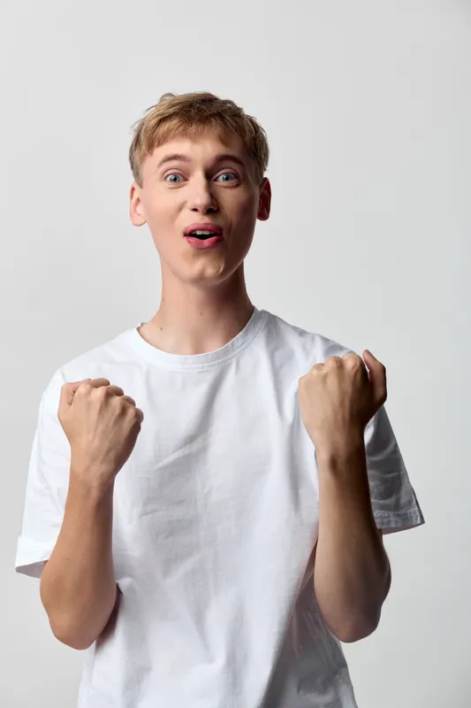 Excited surprised fist pump celebration youth energy expression white t shirt enthusiasm gesture emotion pose victory happiness mood dynamic studio candid upbeat cheerful athletic youthfulness fun