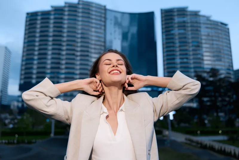 Confident woman in business attire enjoying urban scenery with skyscrapers, expressing joy and empowerment in a professional environment.