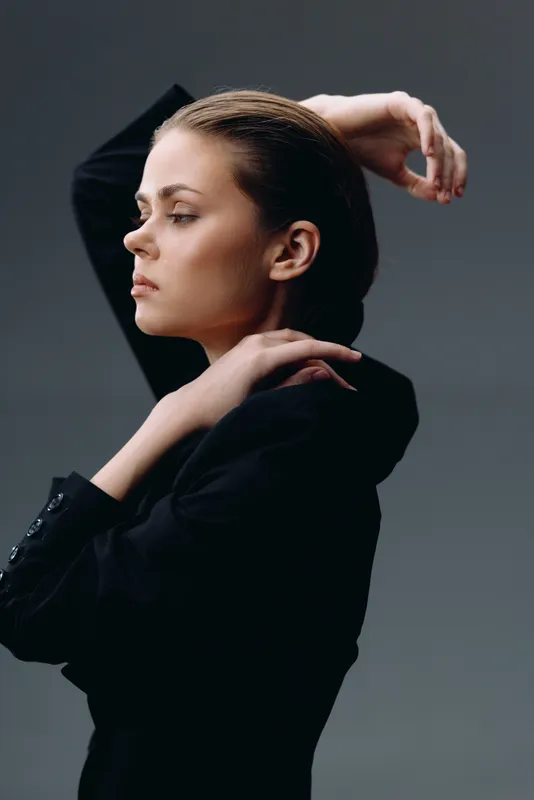 serious woman in black outfit posing with folded arms against neutral background