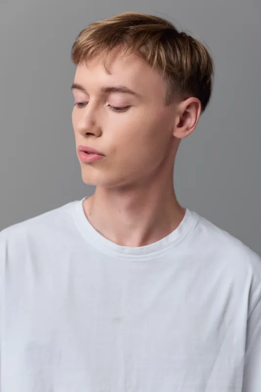 Young man, white tee, calm expression, gray background, studio style with soft lighting and clean lines, suitable for fashion, lifestyle, editorial use and minimalist communication