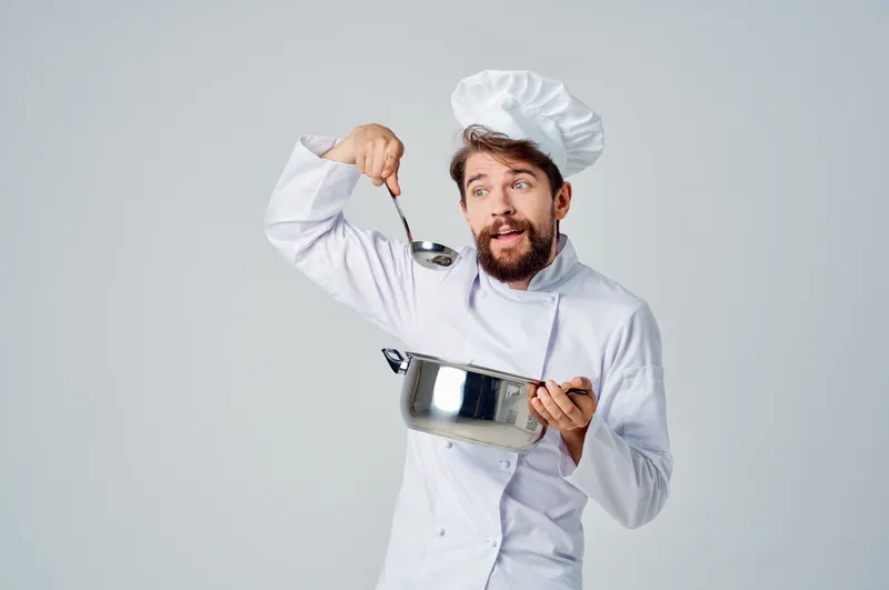 Шеф-повар с кастрюлей в руках на кухне ресторана занимается приготовлением еды