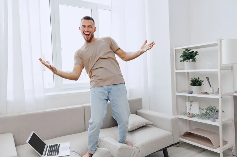 Happy man celebrating at home, embracing solo living and emotional minimalism, expressing joy in a cozy environment with soft colors and natural light.