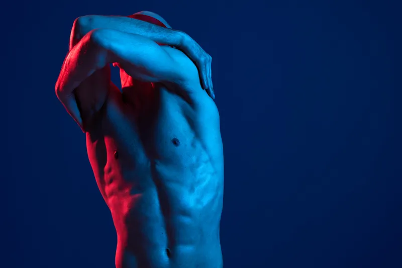 Muscular man posing in dynamic motion, showcasing strong physique with dramatic lighting, blue and red colors enhance the visual impact.