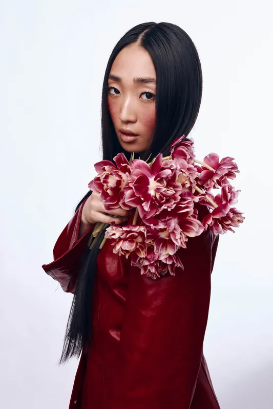 Женщина с длинными черными волосами держит букет розовых цветов в красной куртке в солнечный день