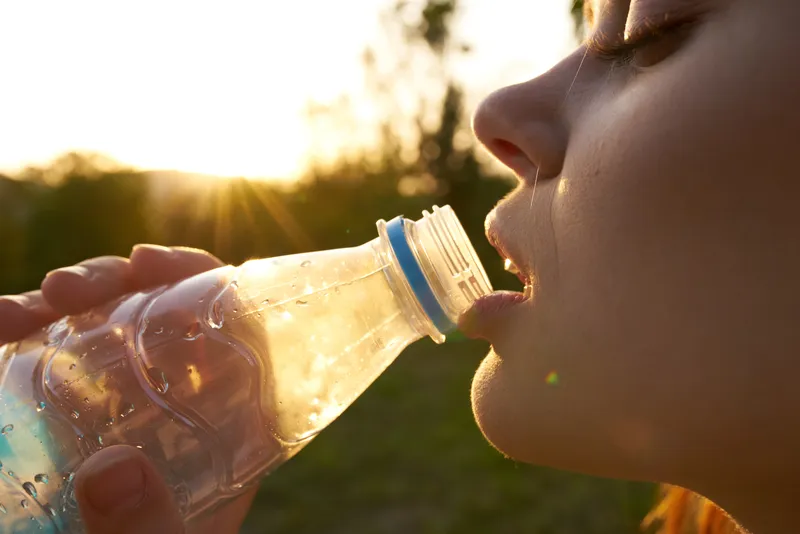 Крупный план лица женщины, пьющей воду из бутылки летом