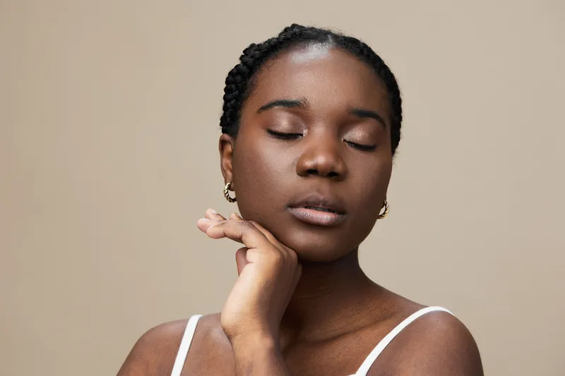 A serene portrait of an African woman with closed eyes expressing tranquility, wearing a simple white top against a soft beige background, showcasing natural beauty and emotion