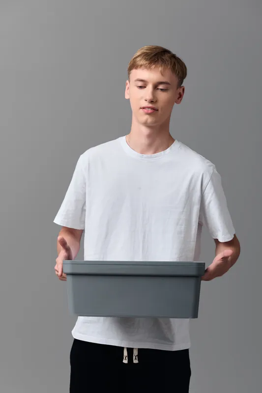 Delivery box held by a young man in a plain studio, illustrating order fulfillment, packaging and logistics in a clear modern setup with focus on handling and warehousing